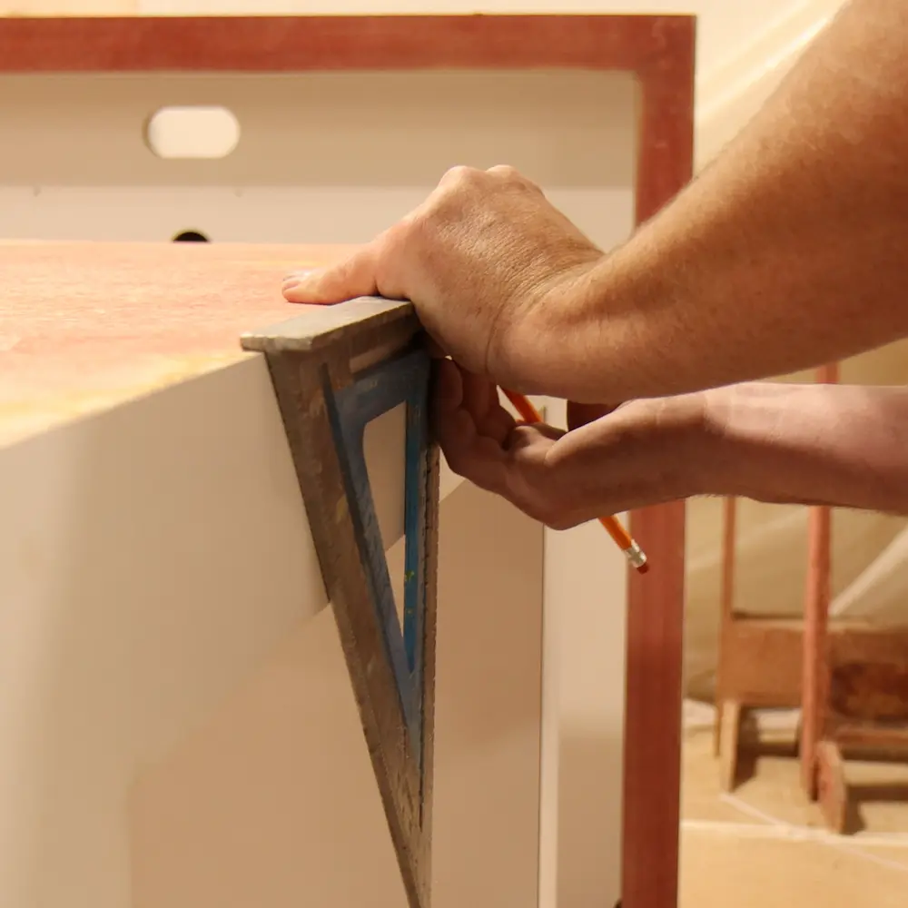 A craftsman using a carpenter's square and pencil to precisely measure a wooden display frame in a workshop, showcasing SoftSpace's ability to build custom trade show exhibits and national programs on tight event timelines.